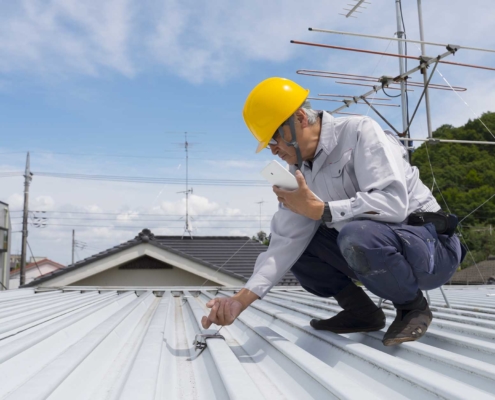 Professional roofer inspecting roof with a yellow hard hat on